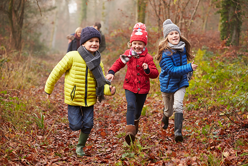 Vier Kinder in bunten Winterjacken laufen durch den Wald.